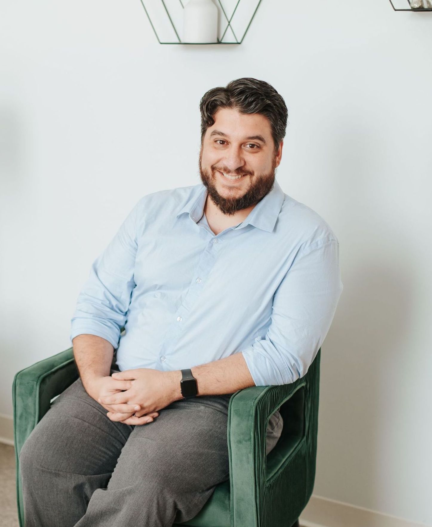 A man with a beard is sitting in a green chair and smiling.