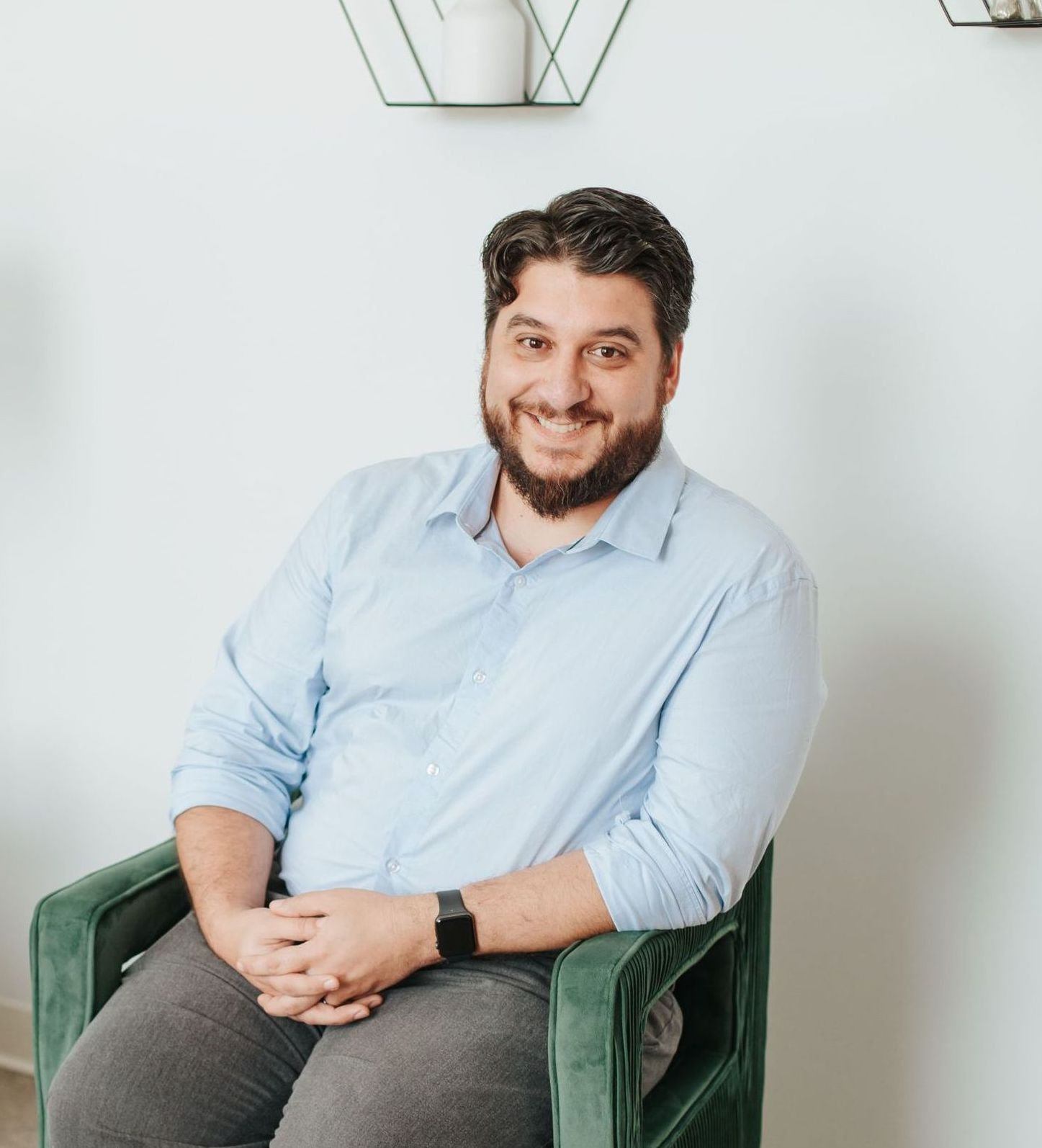 A man with a beard is sitting in a green chair and smiling.