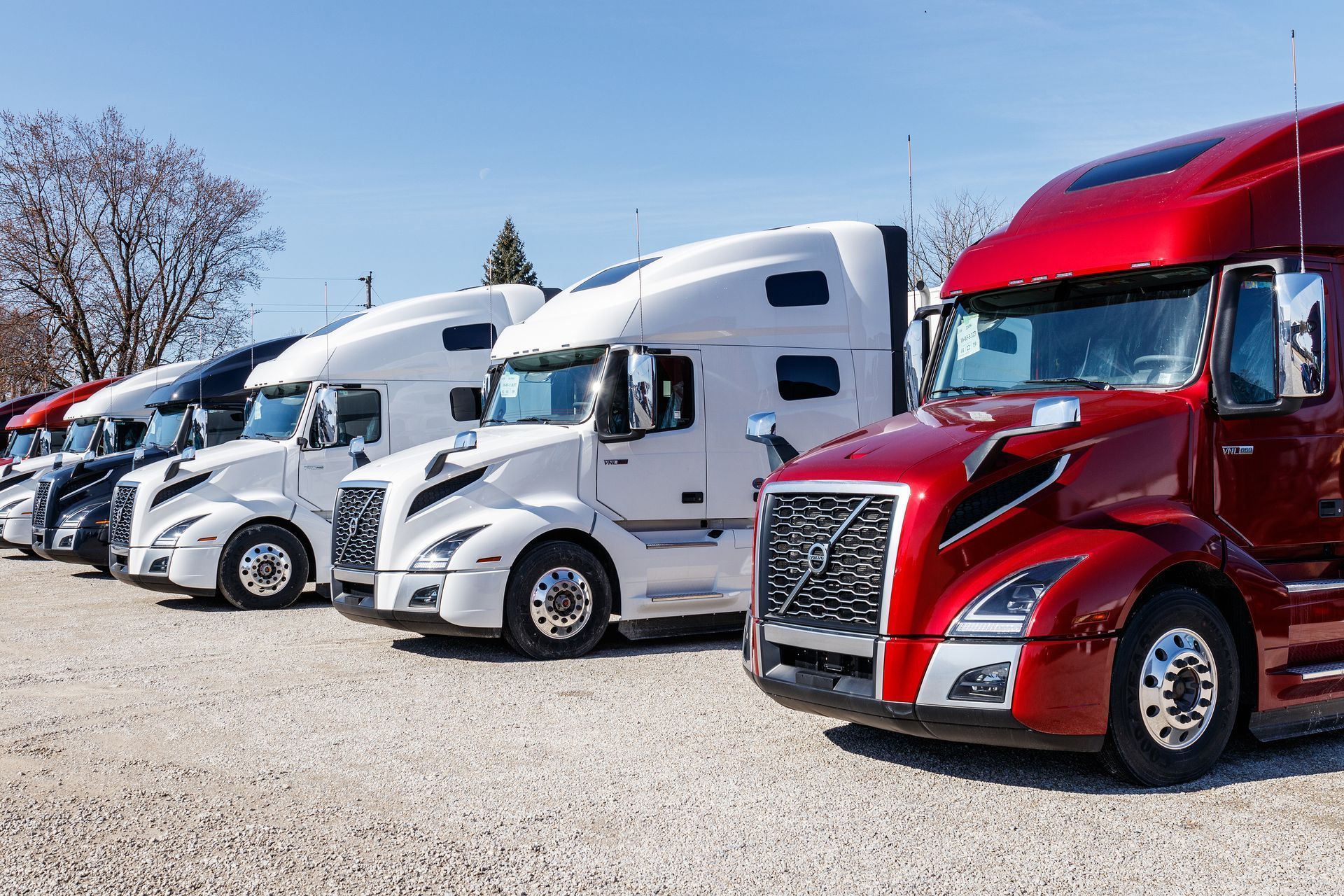 A row of semi trucks are parked in a gravel lot.