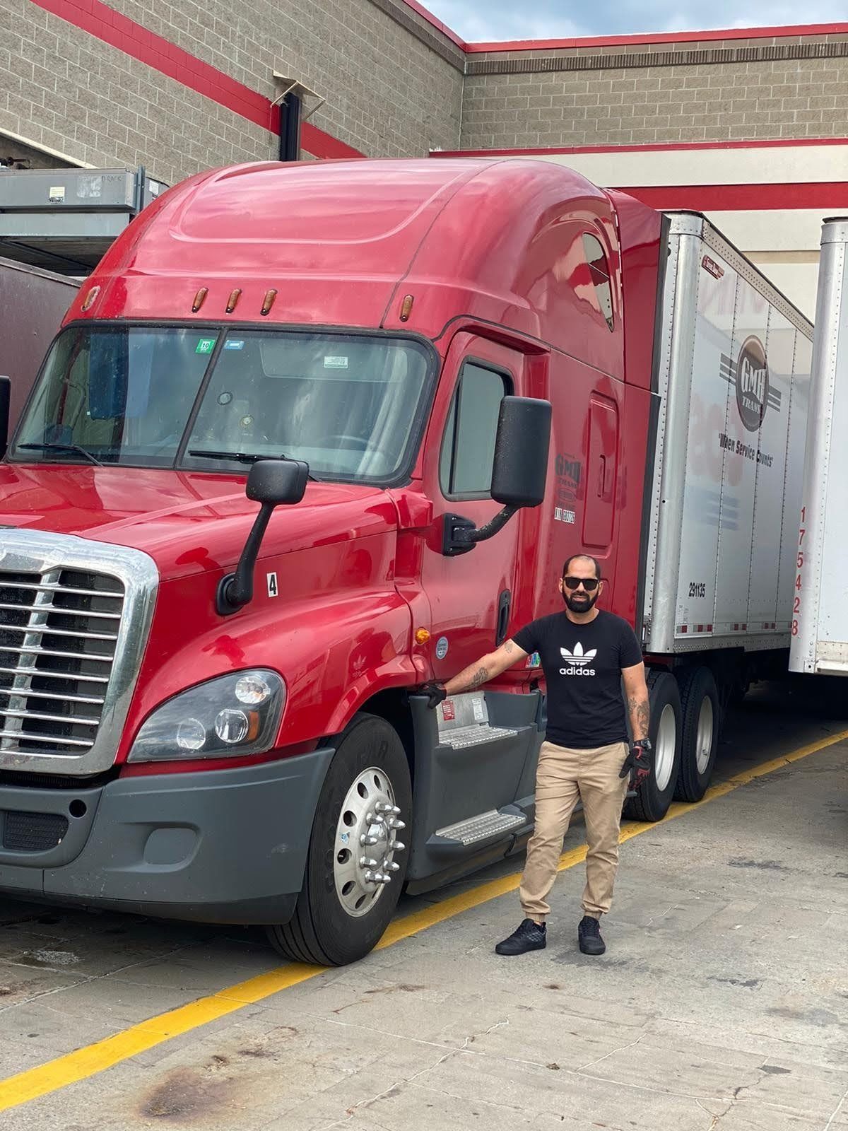 A man is standing in front of a red semi truck.