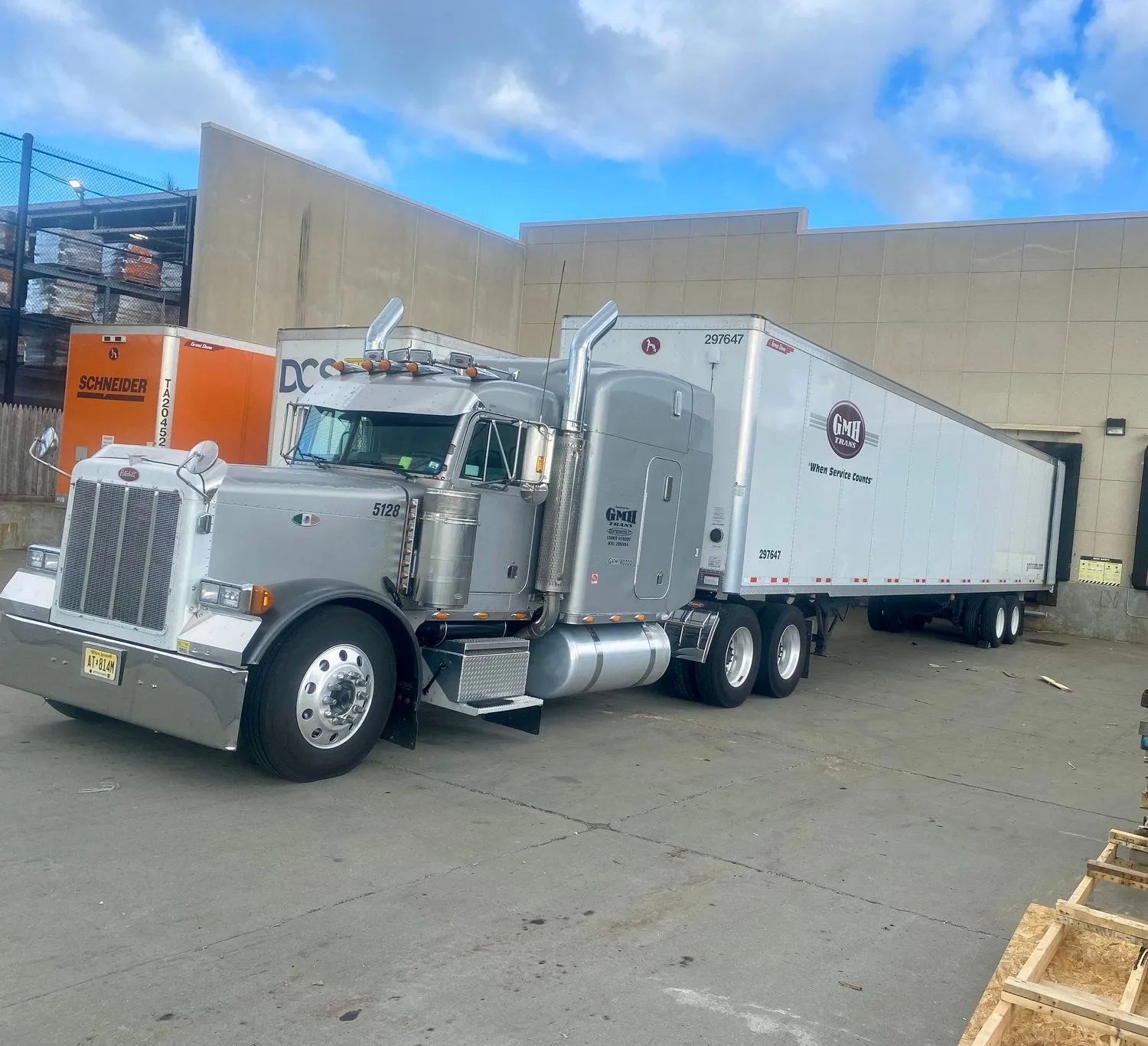 White semi-truck with trailer parked in a lot under a partly cloudy sky.