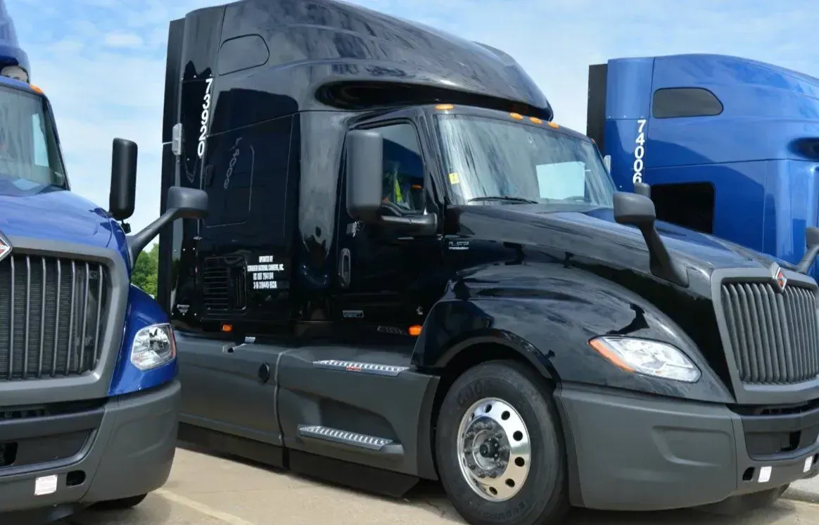 A black semi truck is parked next to a blue semi truck.