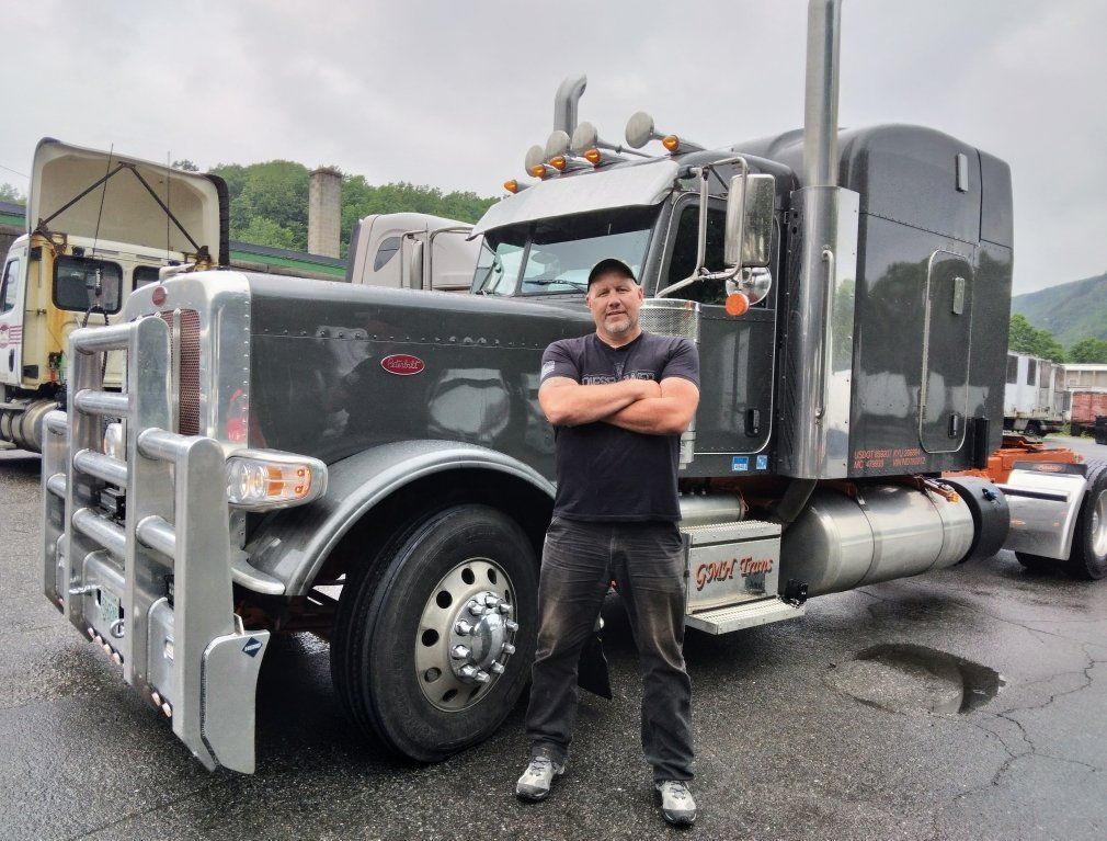 A man is standing in front of a semi truck with his arms crossed.