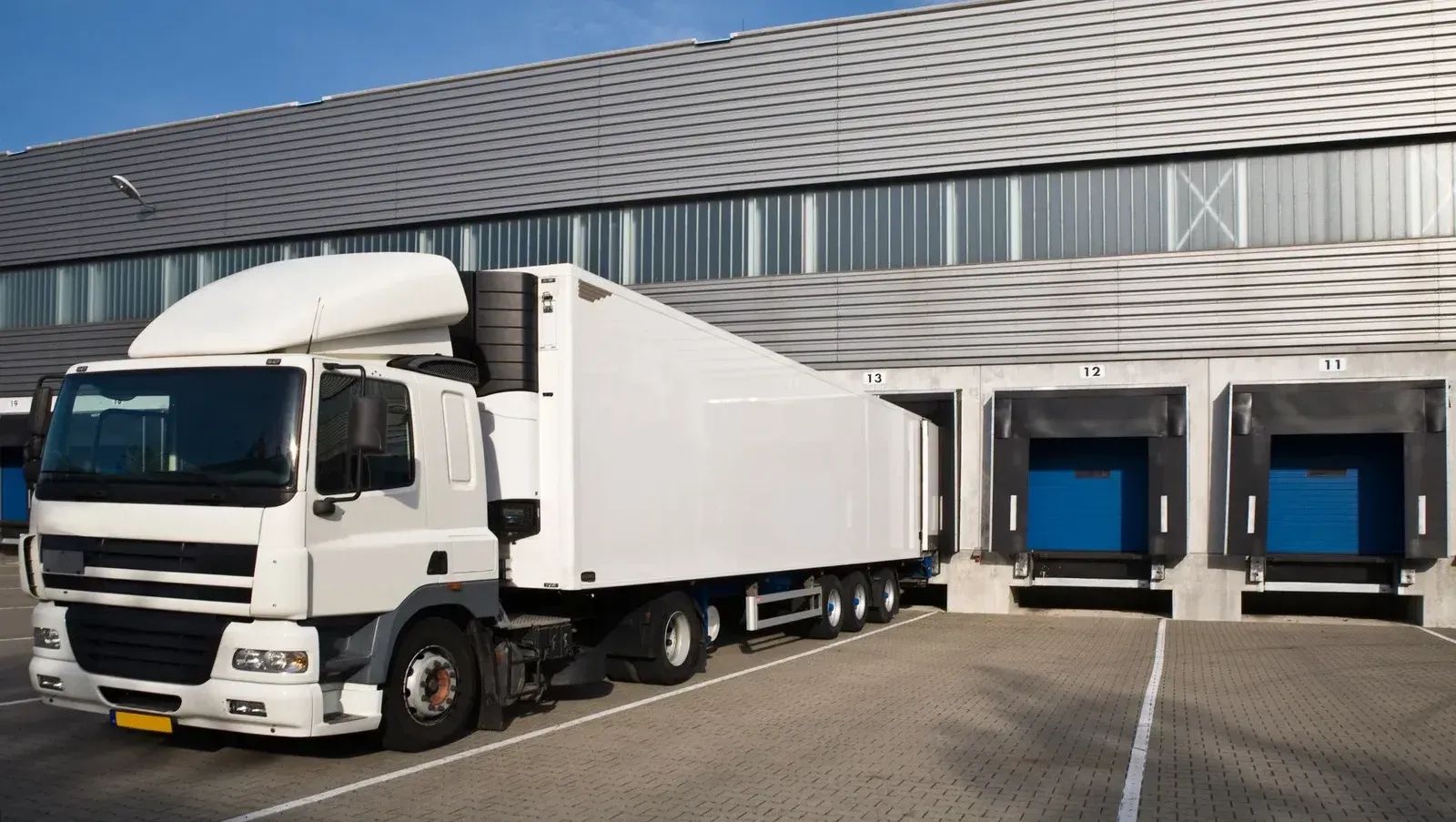 White delivery truck parked at a warehouse loading dock with blue bay doors