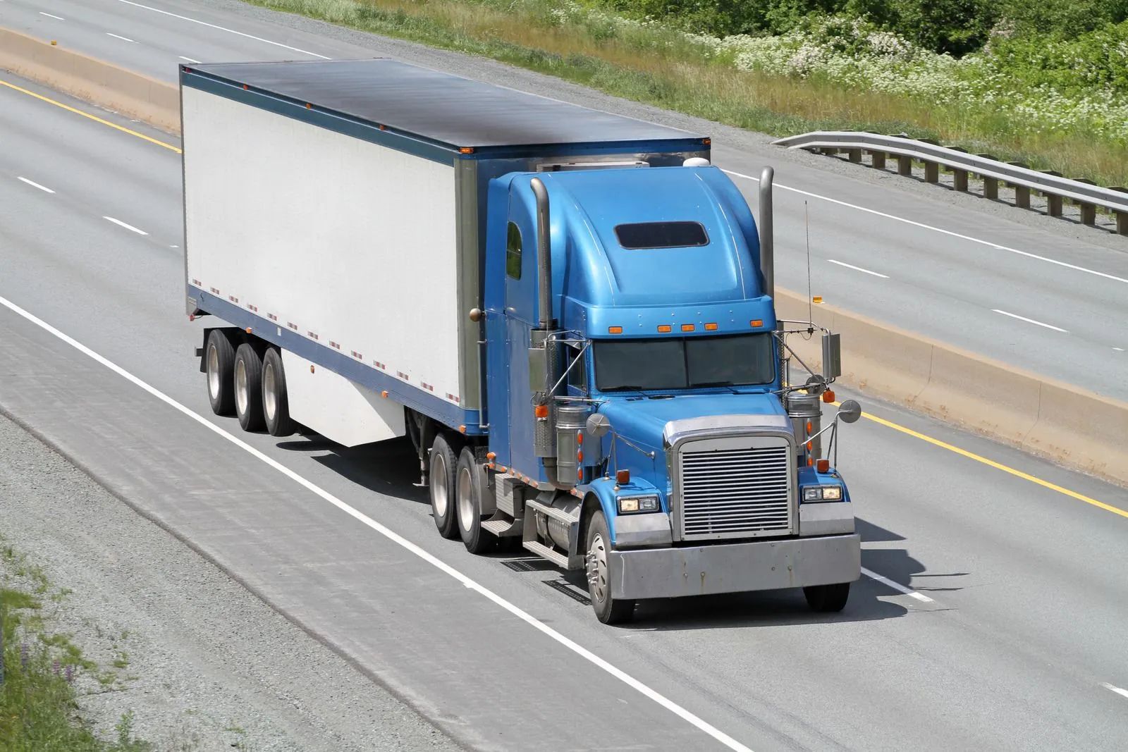 A blue semi-truck with a white trailer drives along a multi-lane highway.
