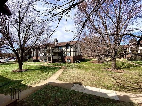 Apartment complex with brick and white trim. Bare trees surround grassy courtyard. Overcast sky.
