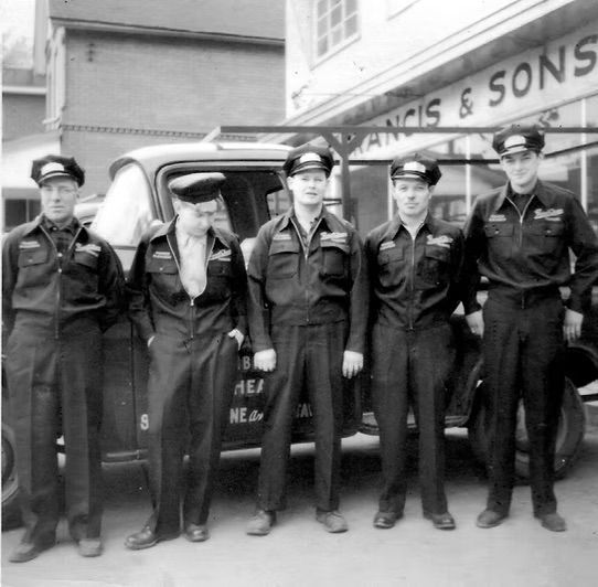 Un groupe d'hommes debout devant un bâtiment sur lequel est écrit Francis & Sons