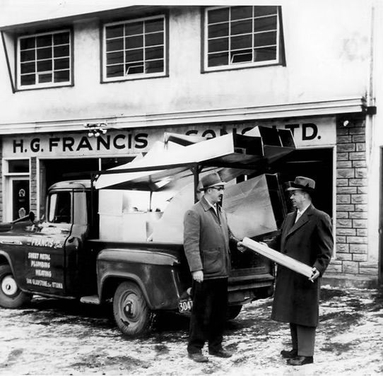 Deux hommes se tiennent devant un bâtiment sur lequel est écrit hg francis