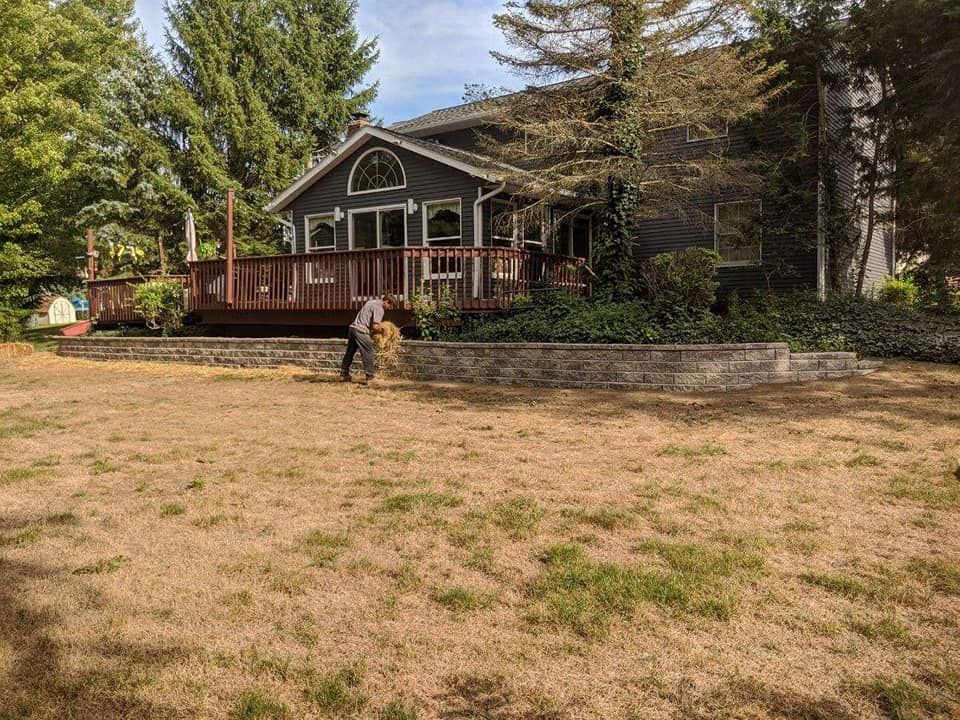 House with deck and dry lawn; person raking leaves in the yard.