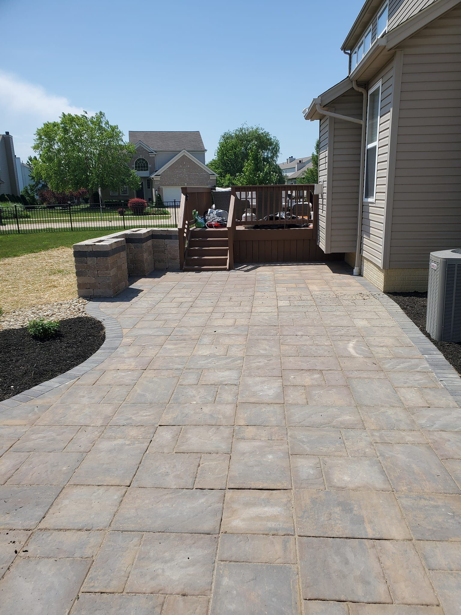 Stone patio with dark mulch border, leading to a wooden deck attached to a house.