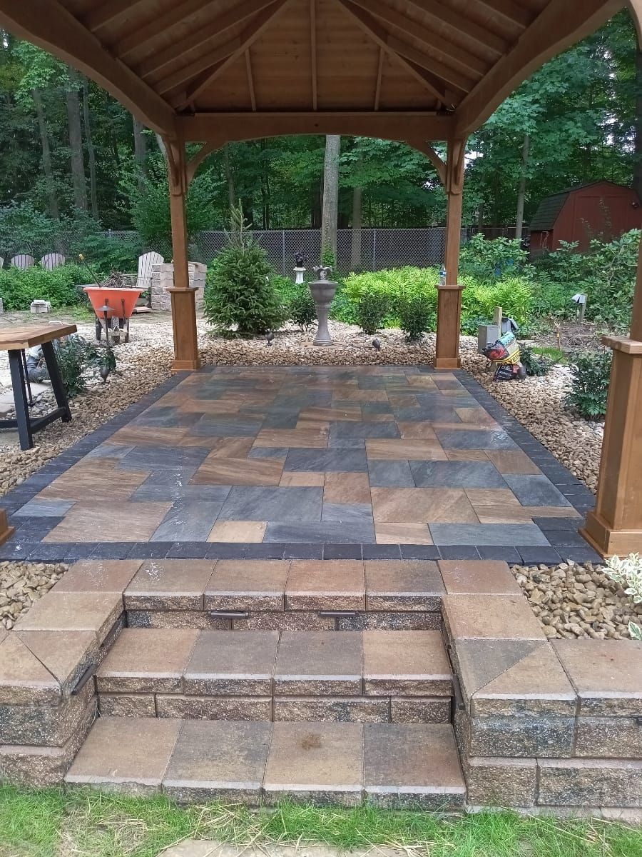 Wooden gazebo over a brick patio with steps. Landscaped backyard with trees.