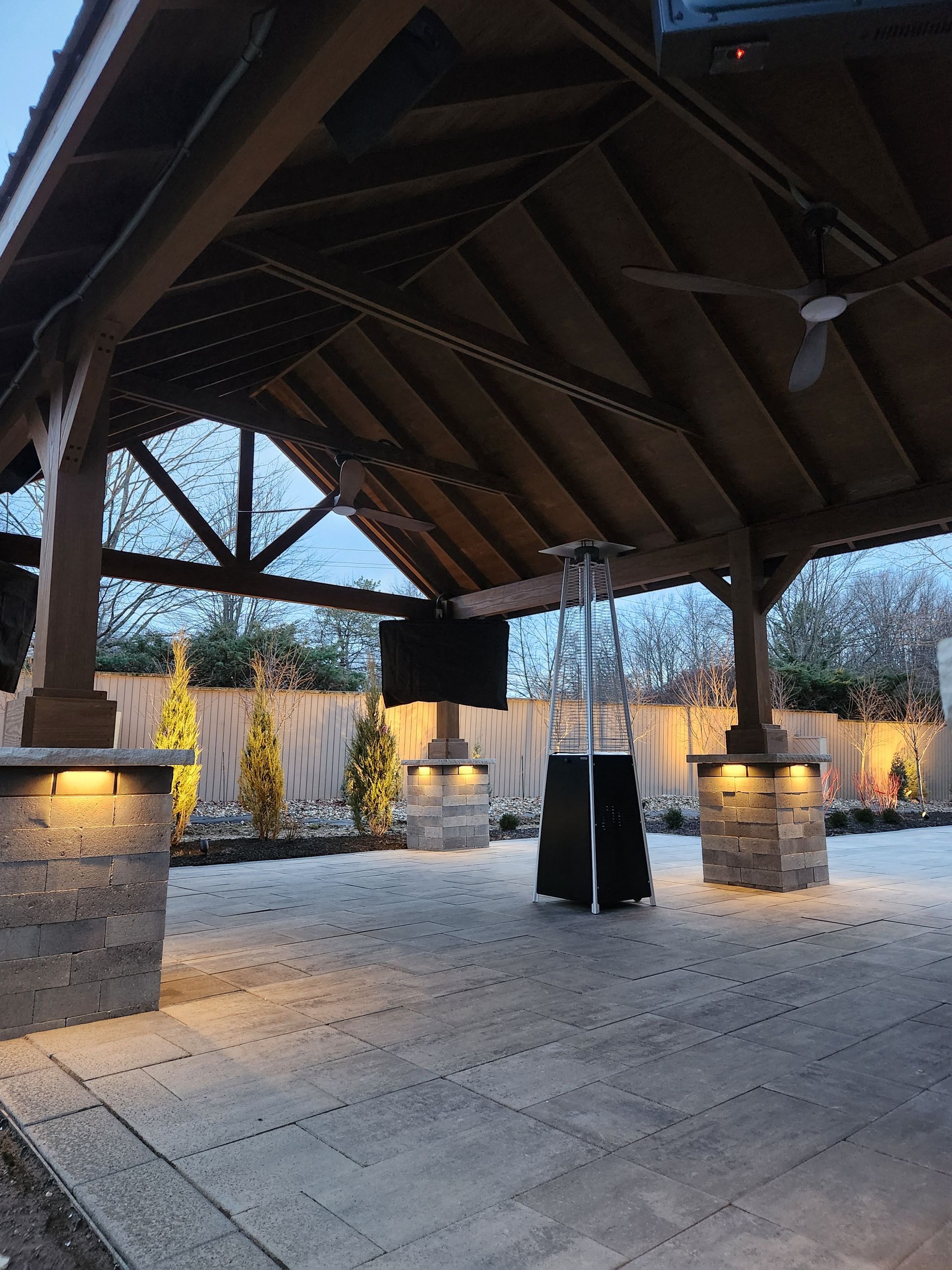 Outdoor patio with stone columns, overhead wooden structure, TV, and a patio heater.