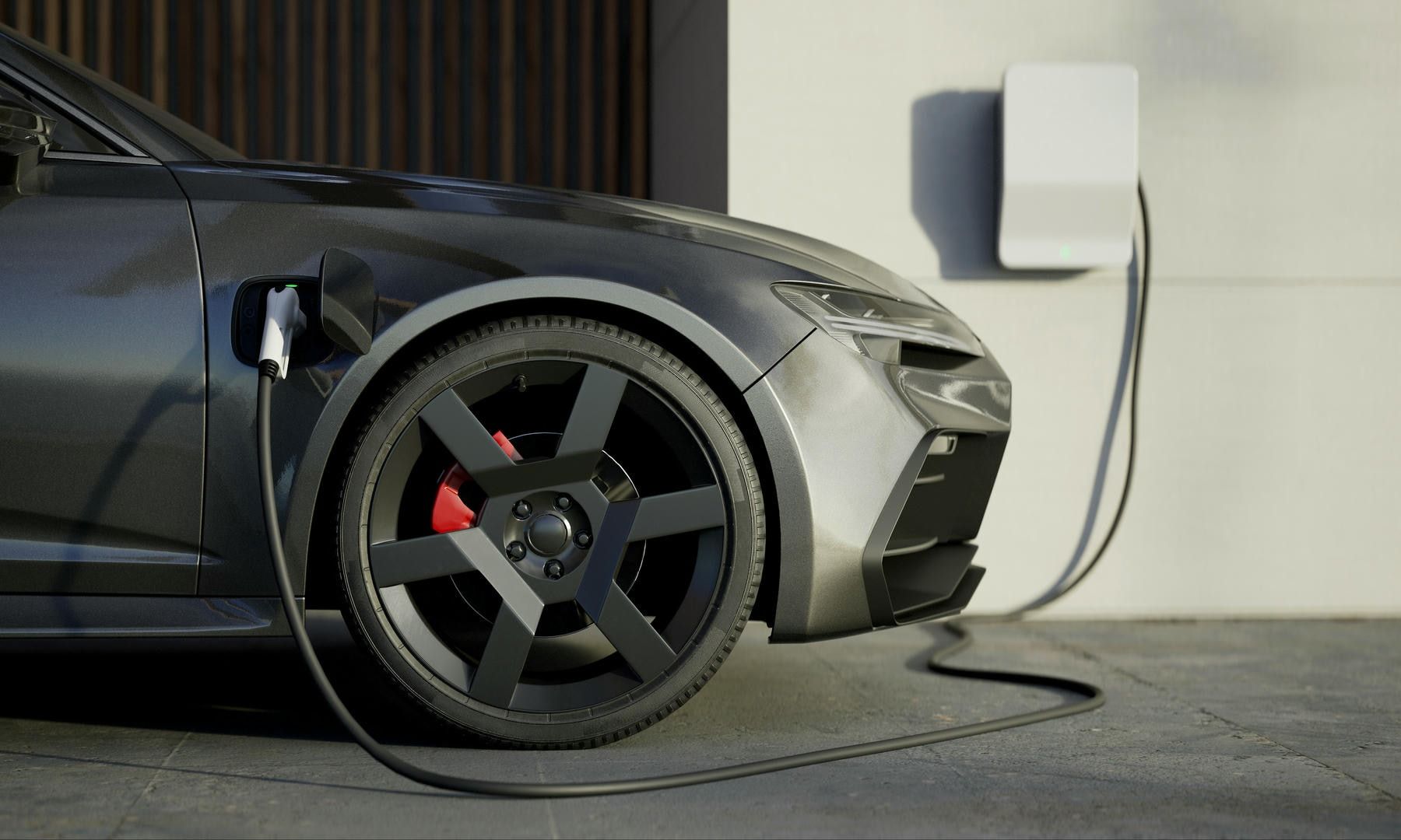 Grey electric car charging at a wall-mounted charging station.