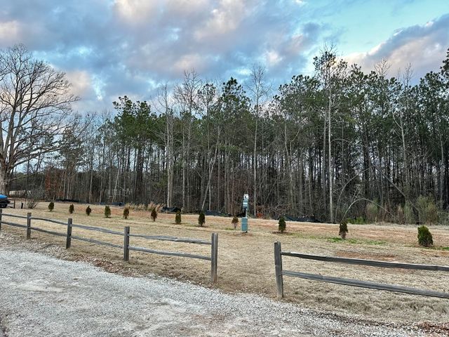 A wooden fence surrounds a field with trees in the background.