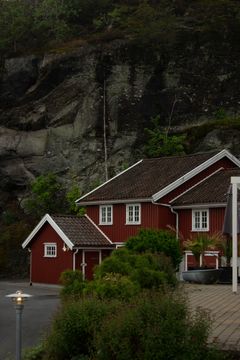 Red houses with white trim at the base of a dark, mossy cliff with a thin waterfall.