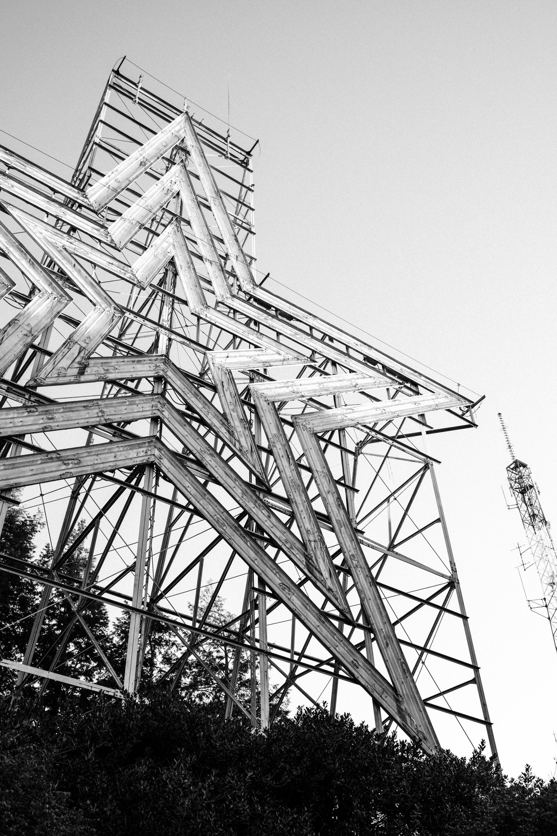 Black-and-white view of a large metal electrical transmission tower against the sky.
