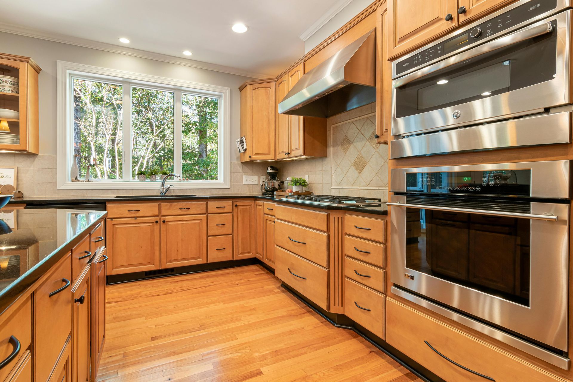 Bright modern kitchen with wooden cabinets, stainless steel appliances, and a window over the sink.