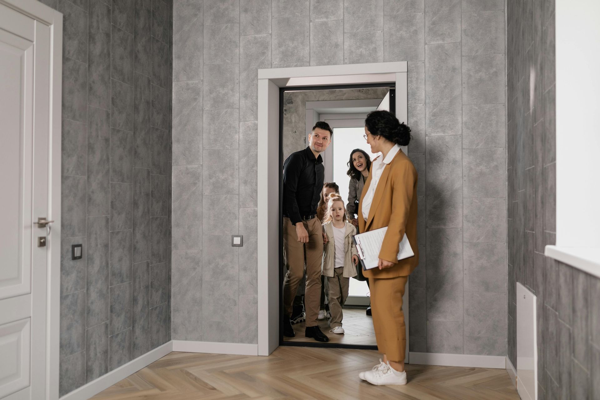 Three people standing in a doorway of an empty room with gray wallpaper and wood floors