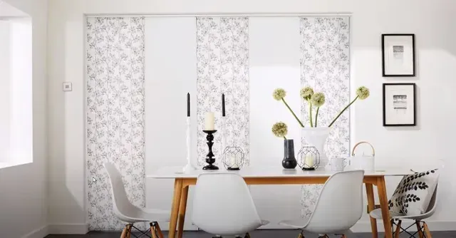 a dining room with a table and chairs and sliding panels on the wall Versatile room solutions patterned panel track shades Love is Blinds Michigan