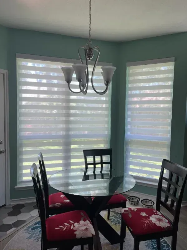 A dining room with a glass table and chairs and a chandelier. Love is Blinds Michigan