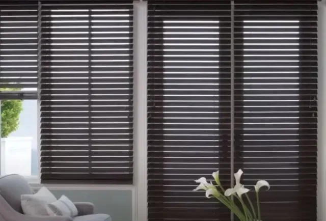 A living room with a couch and a vase of flowers in front of a window with blinds. Love is Blinds Arizona (844) 936-2446