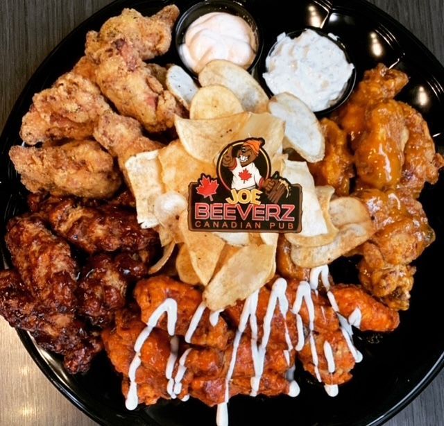 Assorted fried chicken wings and sides on a black platter with dipping sauces and fries.