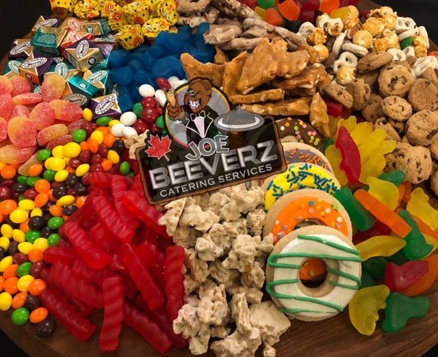 Assorted colorful snacks and cookies arranged on a tray with a Beezer Catering Services logo in the center
