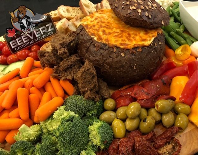 Vegetable and bread platter with a cheese-topped baked dip in a round bread bowl