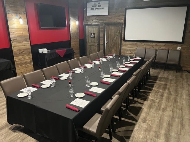 Private dining room with a long set table, black tablecloths, red accents, and a projector screen.