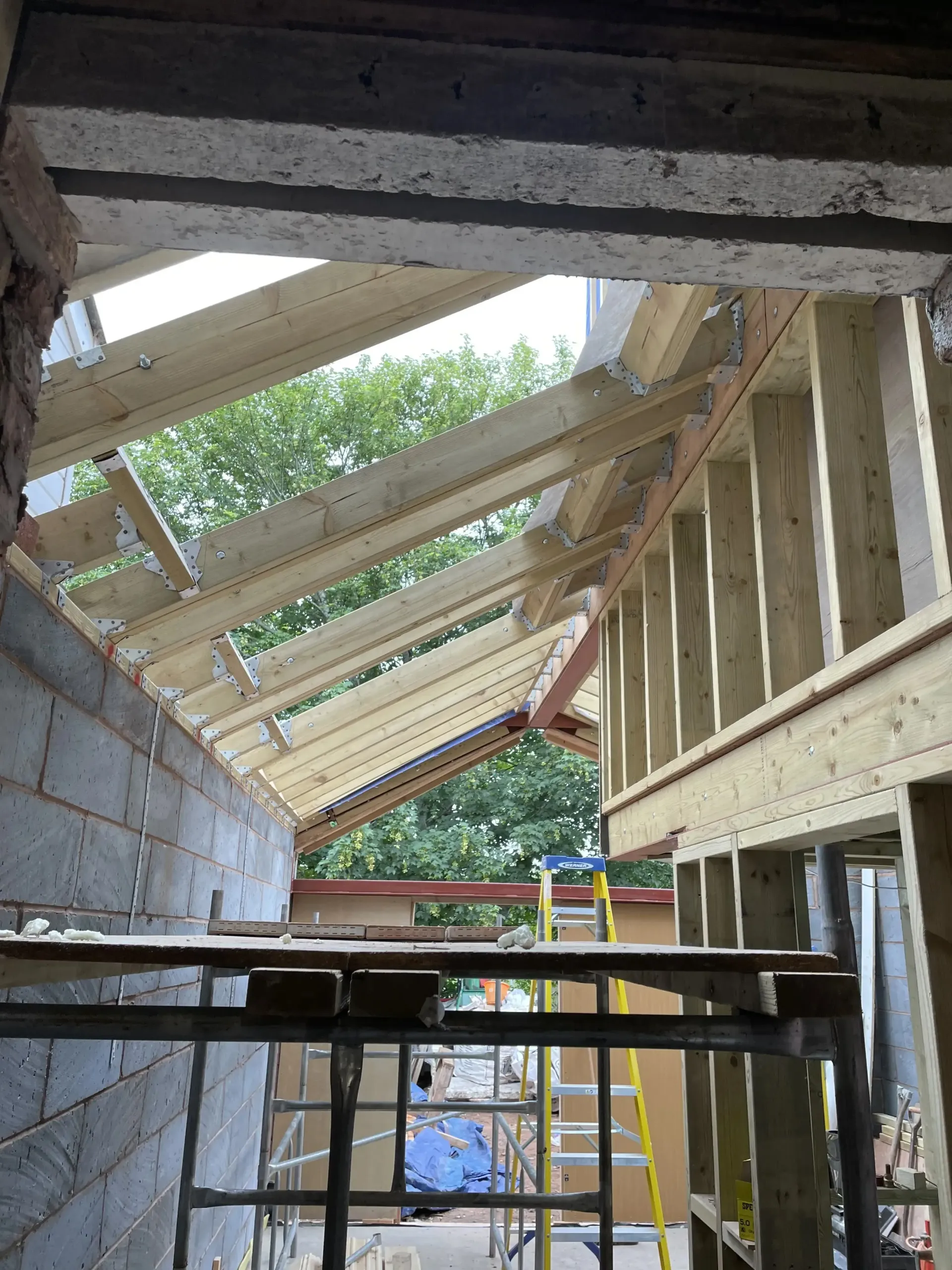 Partially constructed roof framing with exposed beams and scaffolding inside a building site