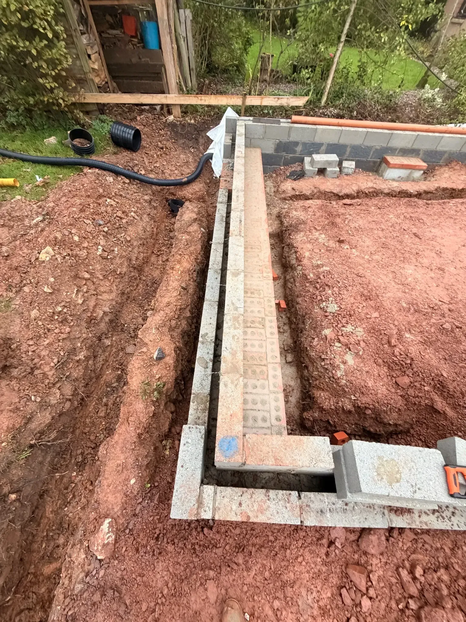 Construction trench with concrete foundation walls and exposed soil, viewed from above