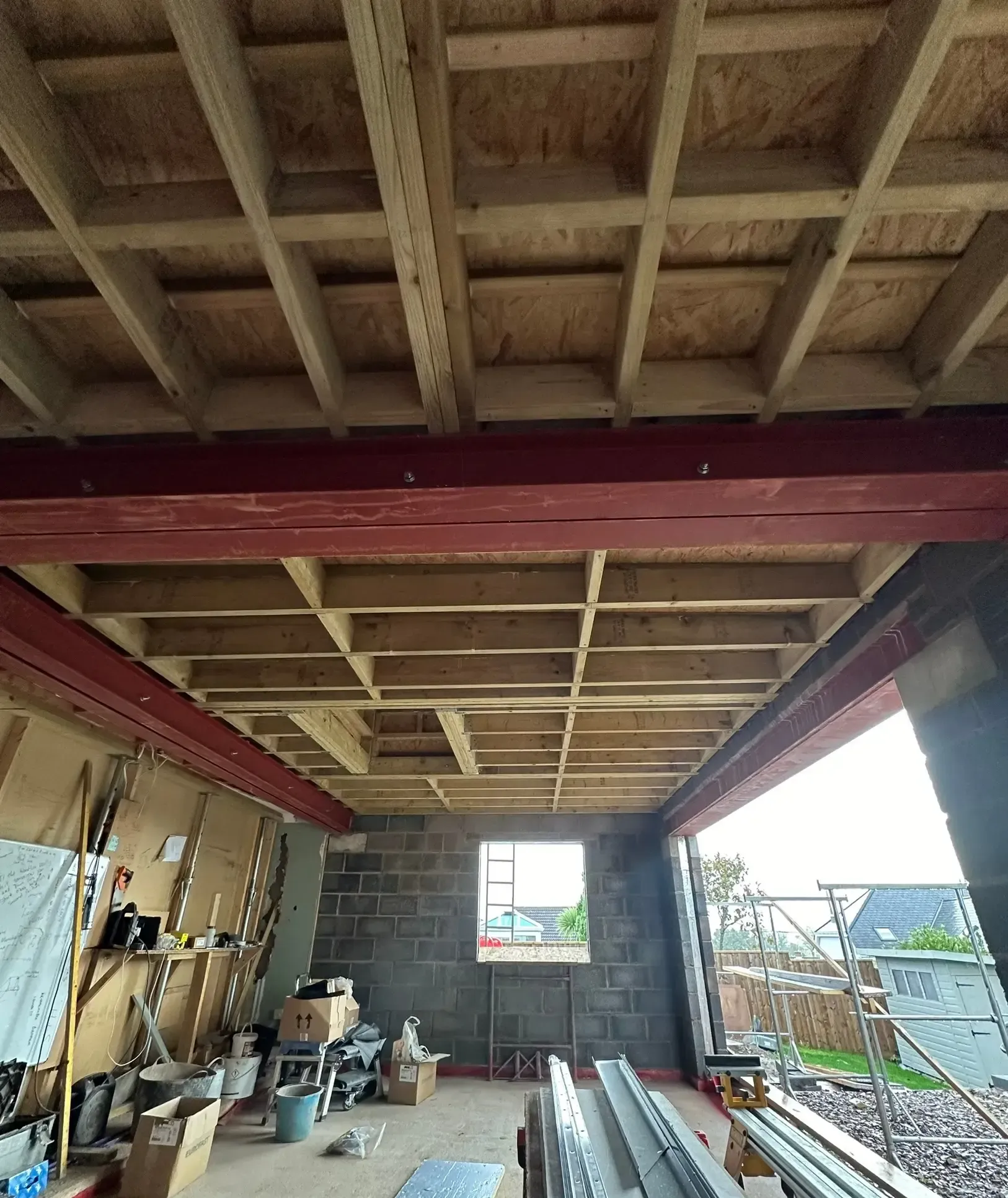 Covered patio under construction with exposed wooden beams, tools, and materials along the sides.