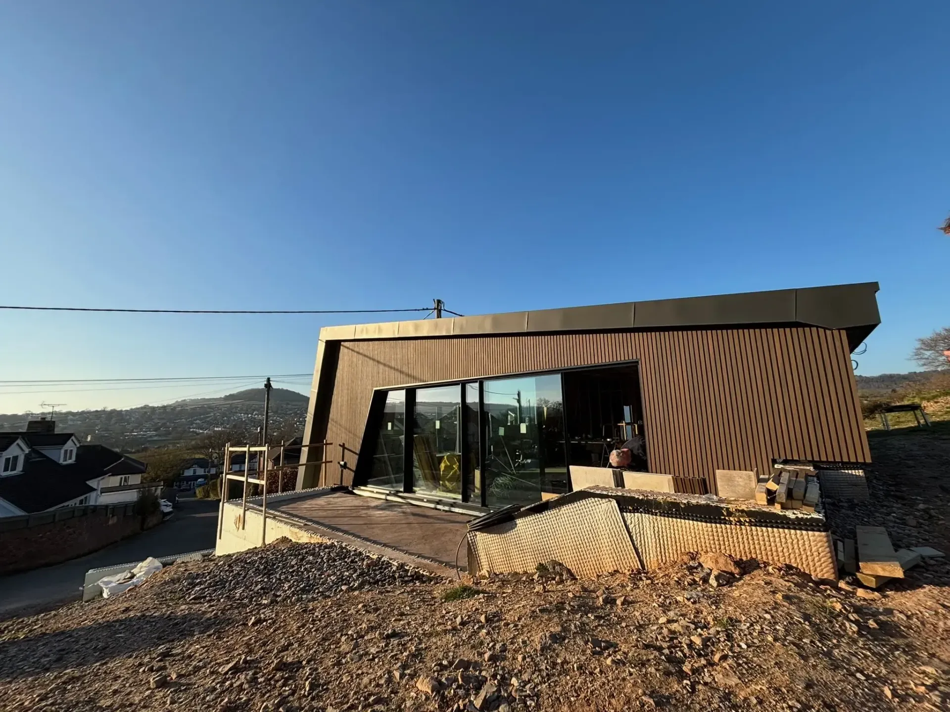 Modern house with slanted wooden facade and large windows on a rocky hillside under a clear blue sky