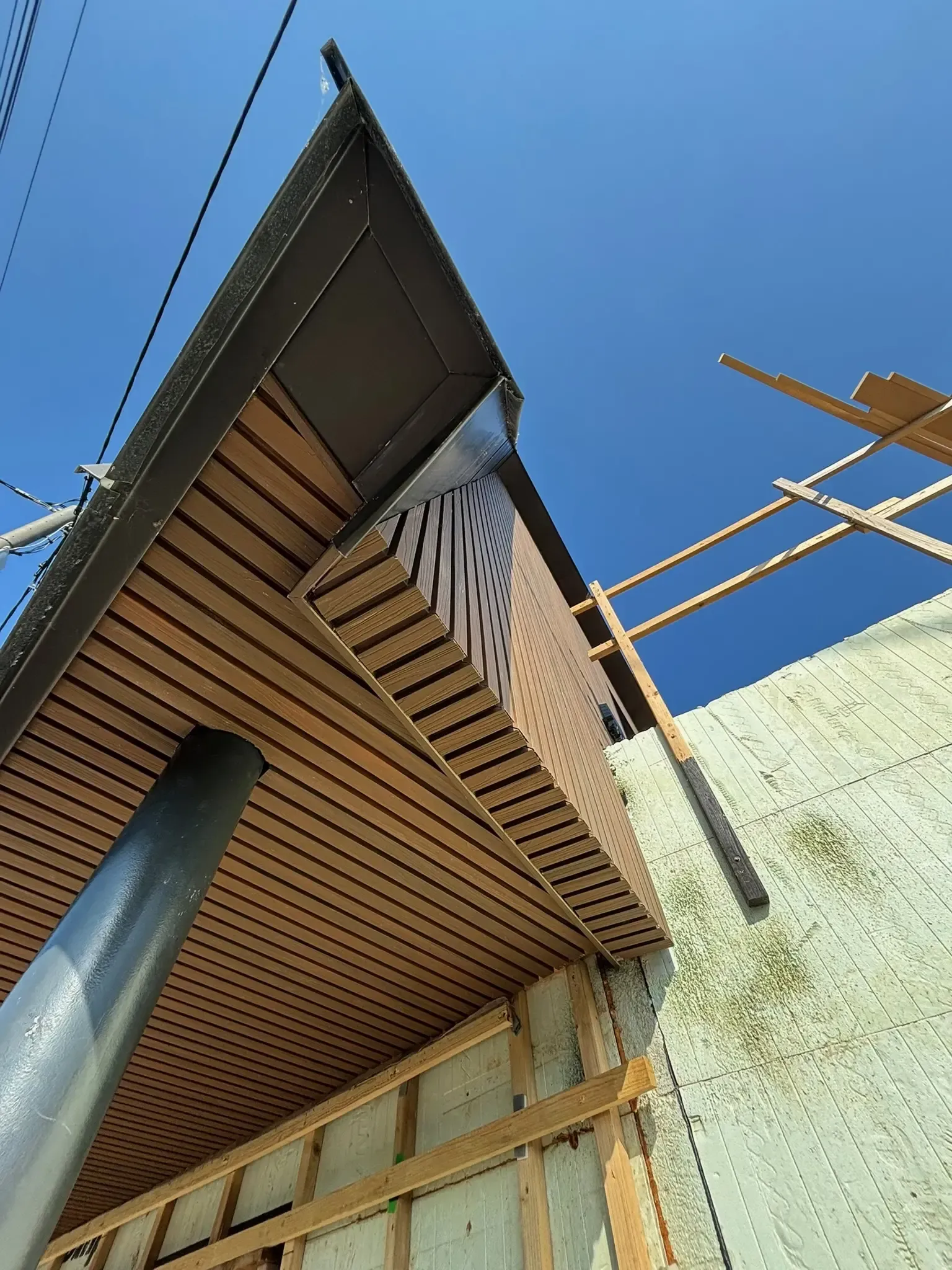 Low-angle view of a wooden house exterior with a blue sky and construction scaffolding nearby