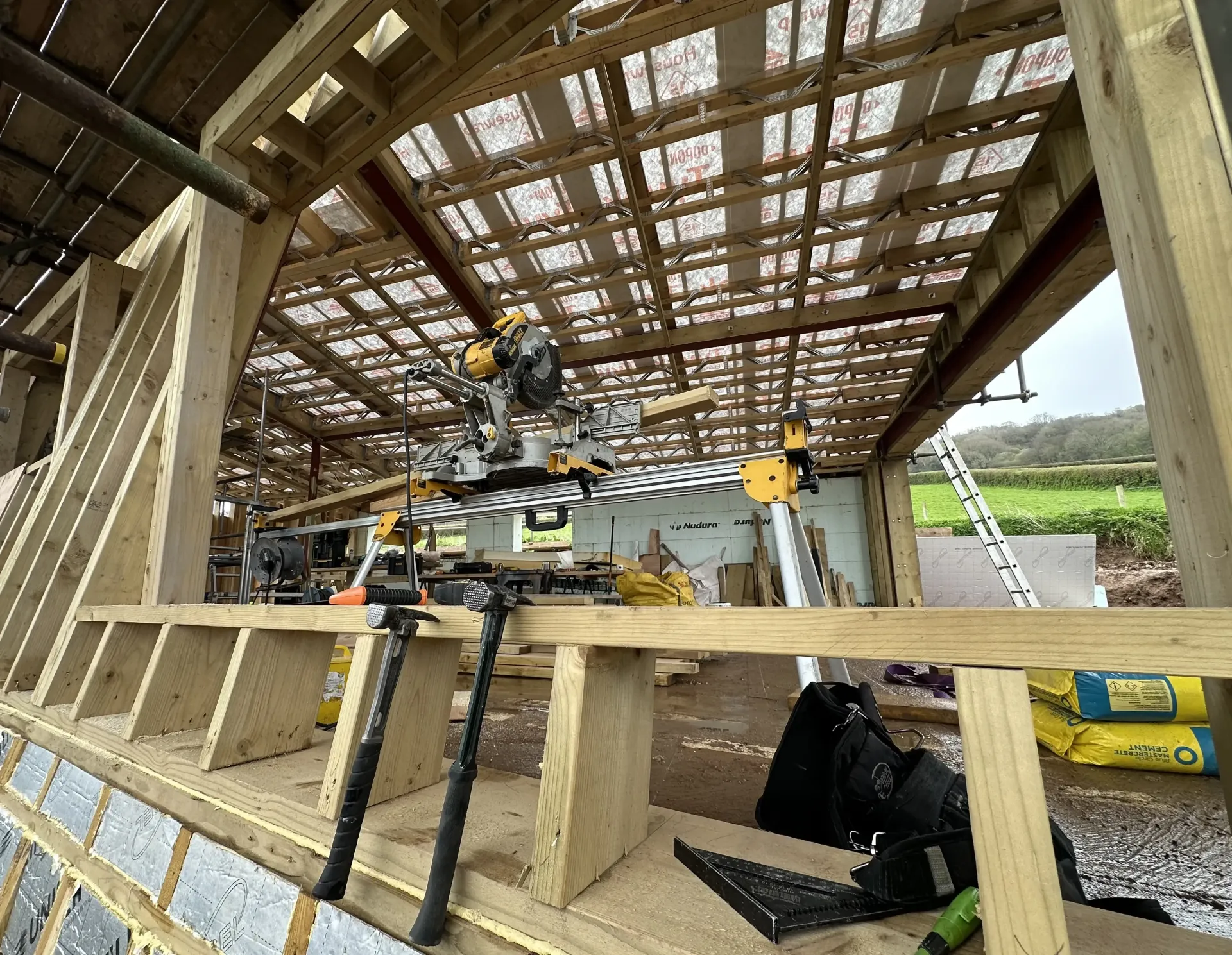 Workers under a wooden canopy using a yellow excavator at a construction site