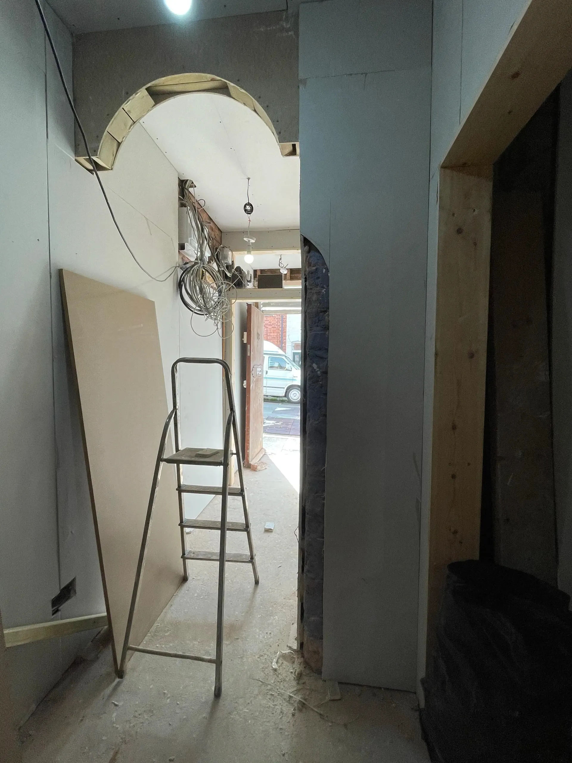 Indoor hallway under renovation with a ladder, exposed ceiling, and a decorative arched opening.