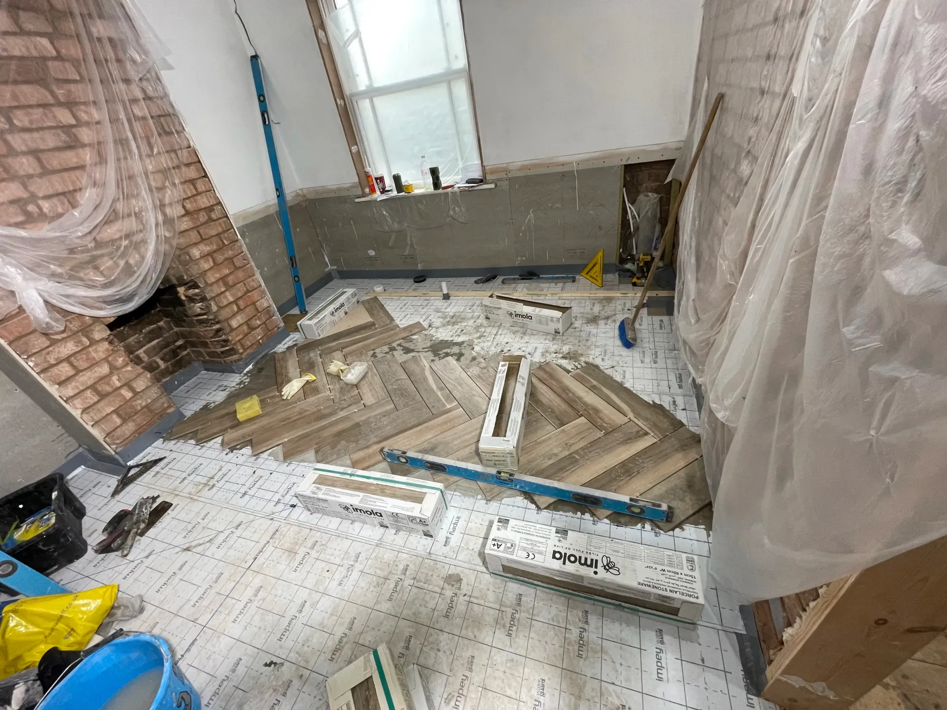 Bathroom under renovation with plastic-covered walls, scattered tiles, and construction debris on the floor