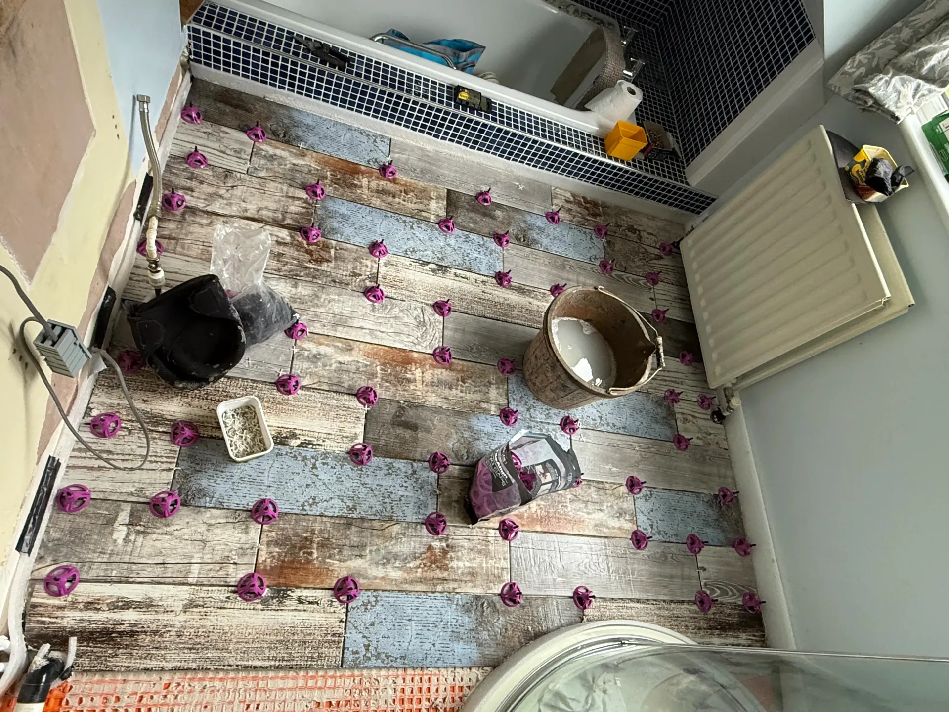 Top-down view of a cat enclosure with blankets, toys, a metal bowl, and a radiator.