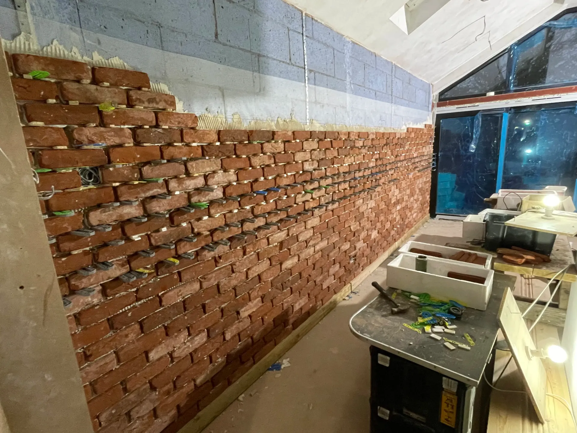 Partially exposed brick wall under renovation beside tables and tools in a bright room