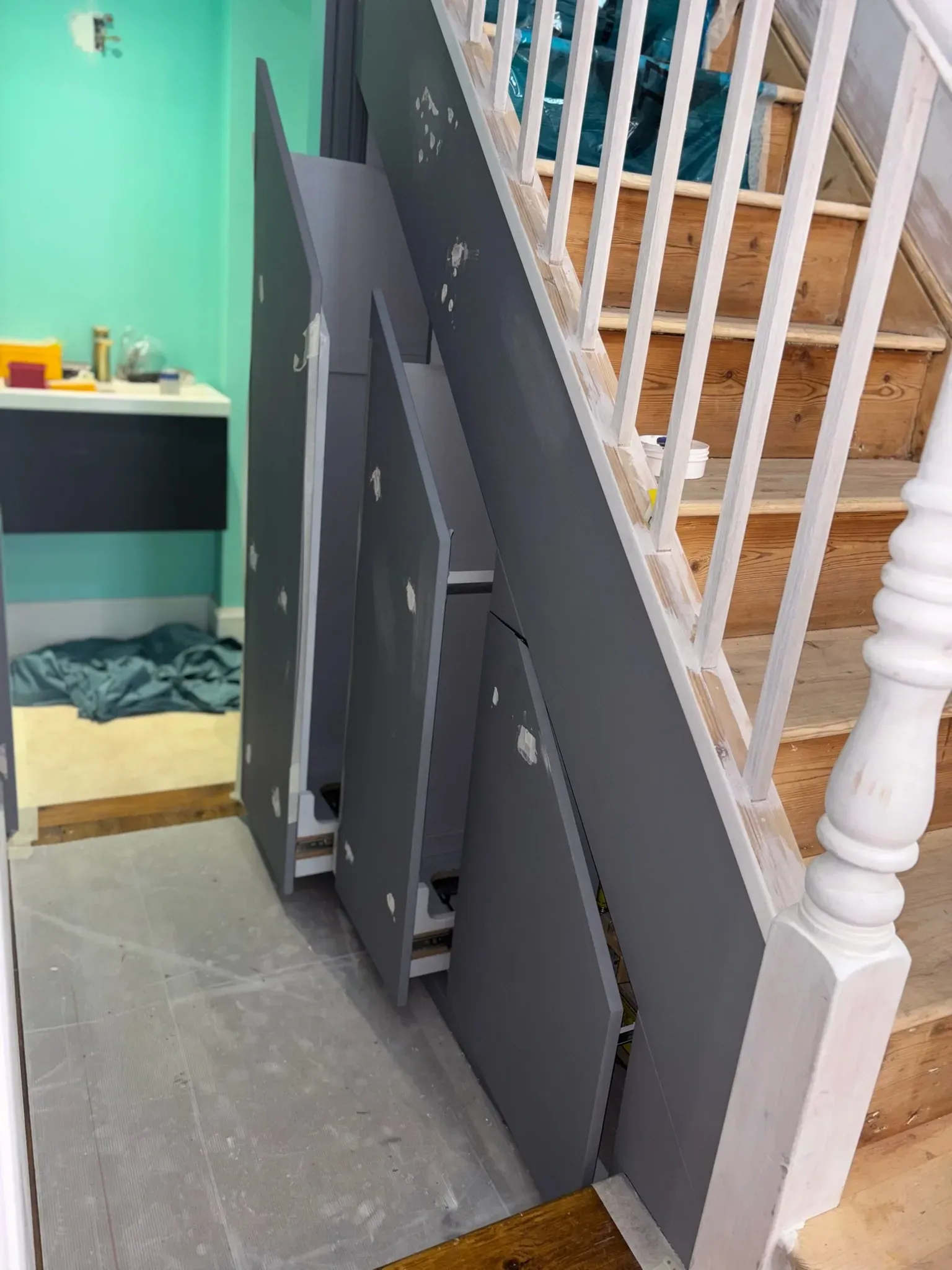 Folded gray wheelchair ramp leaning beside a staircase with white railings indoors