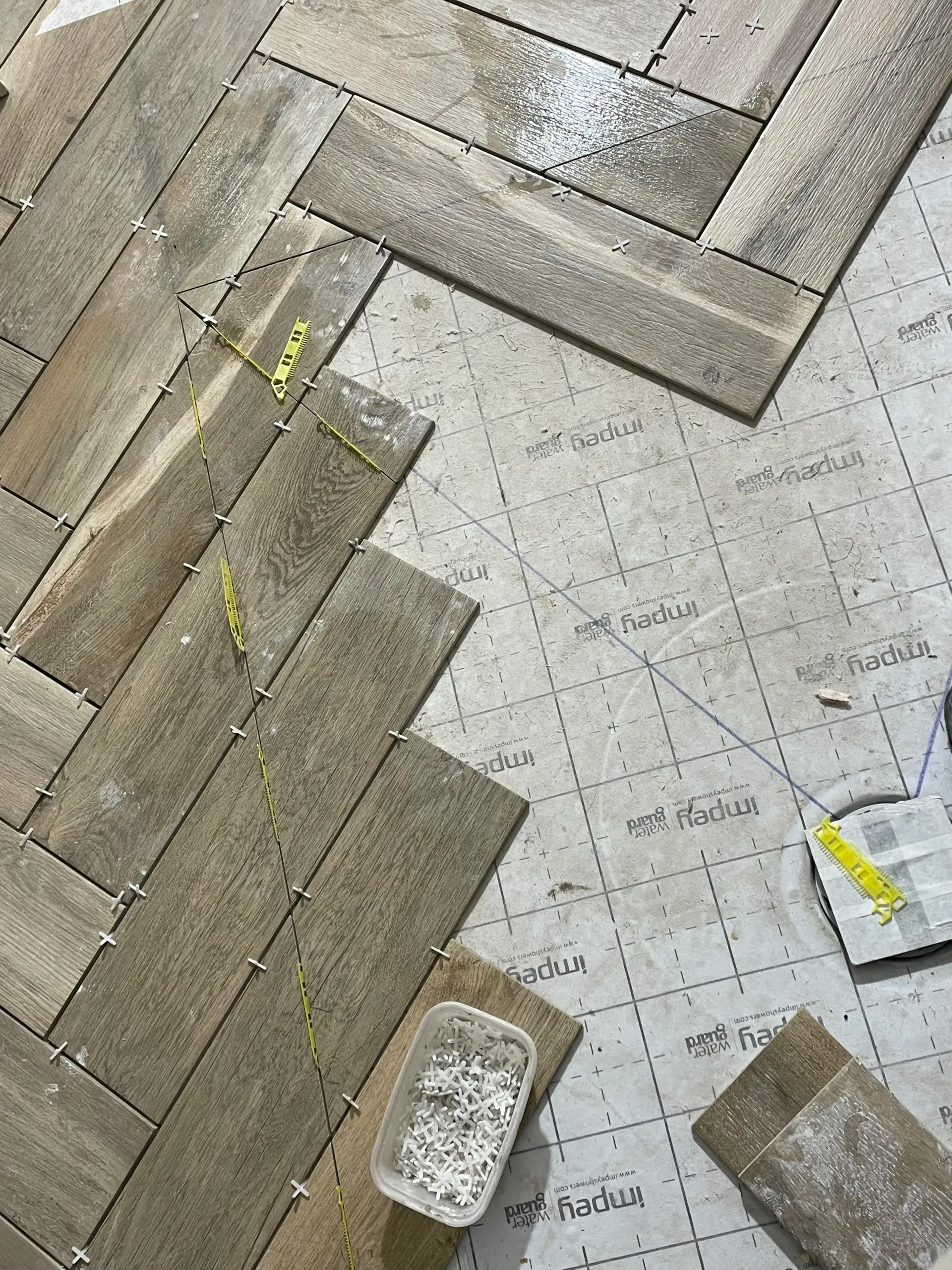 Close-up of diagonal floor tiles with two small adhesive samples and a white sponge on a white surface.