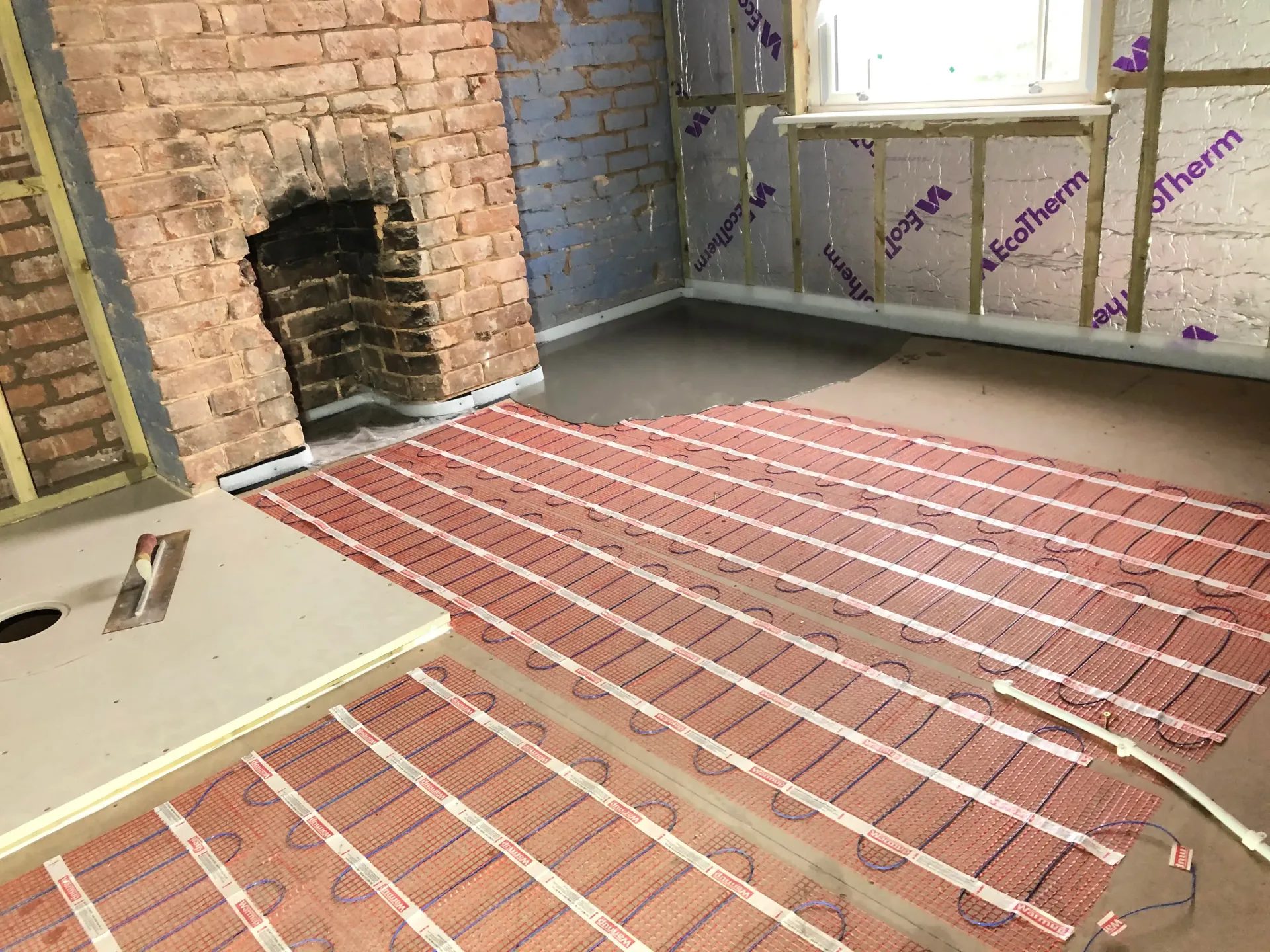 Unfinished room with exposed brick walls, a fireplace, and red striped carpet laid on the floor.