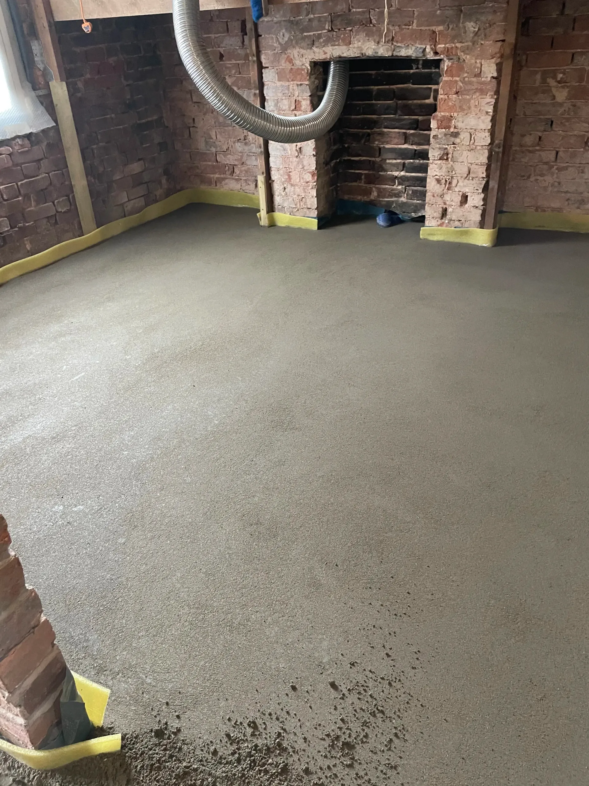 Basement room with wet concrete floor, exposed brick walls, and a central arched brick opening with a hose overhead