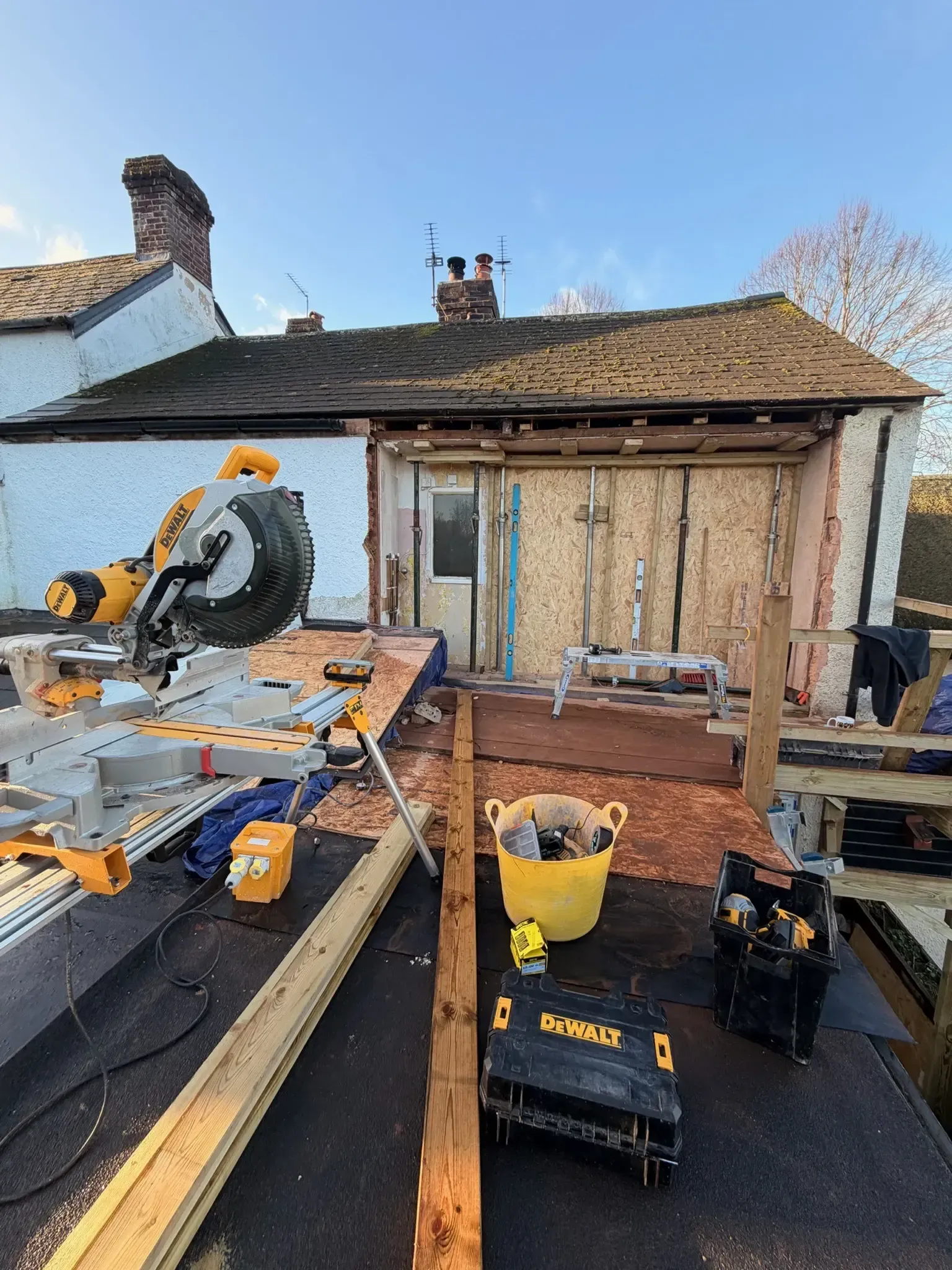 Backyard home renovation with saws, tools, and materials laid out on a roofed patio area