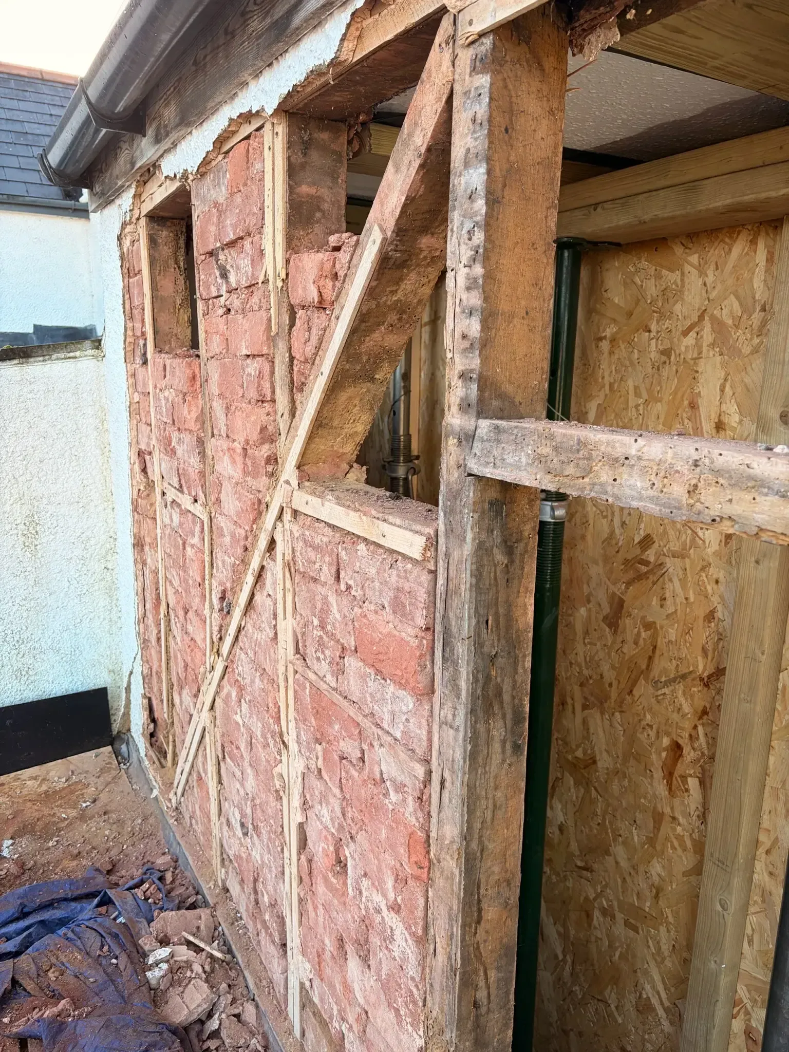 Partially stripped exterior wall under construction with exposed wood framing and pink insulation panels