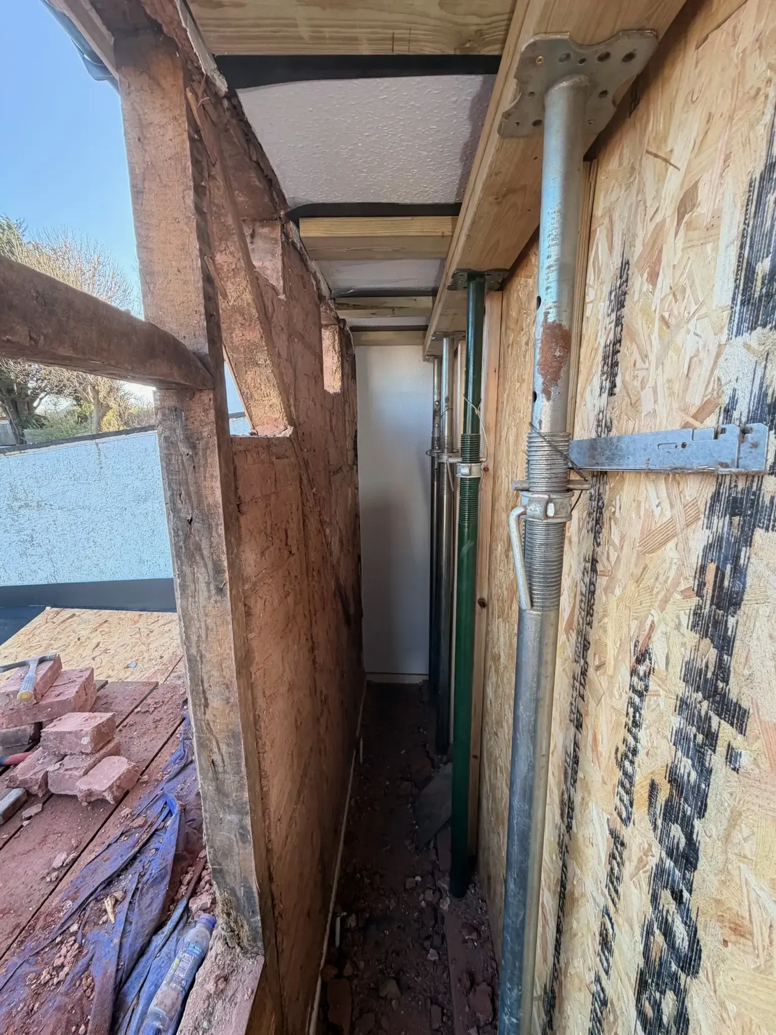 Narrow rooftop walkway with peeling walls, exposed pipes, and debris along the side of a building