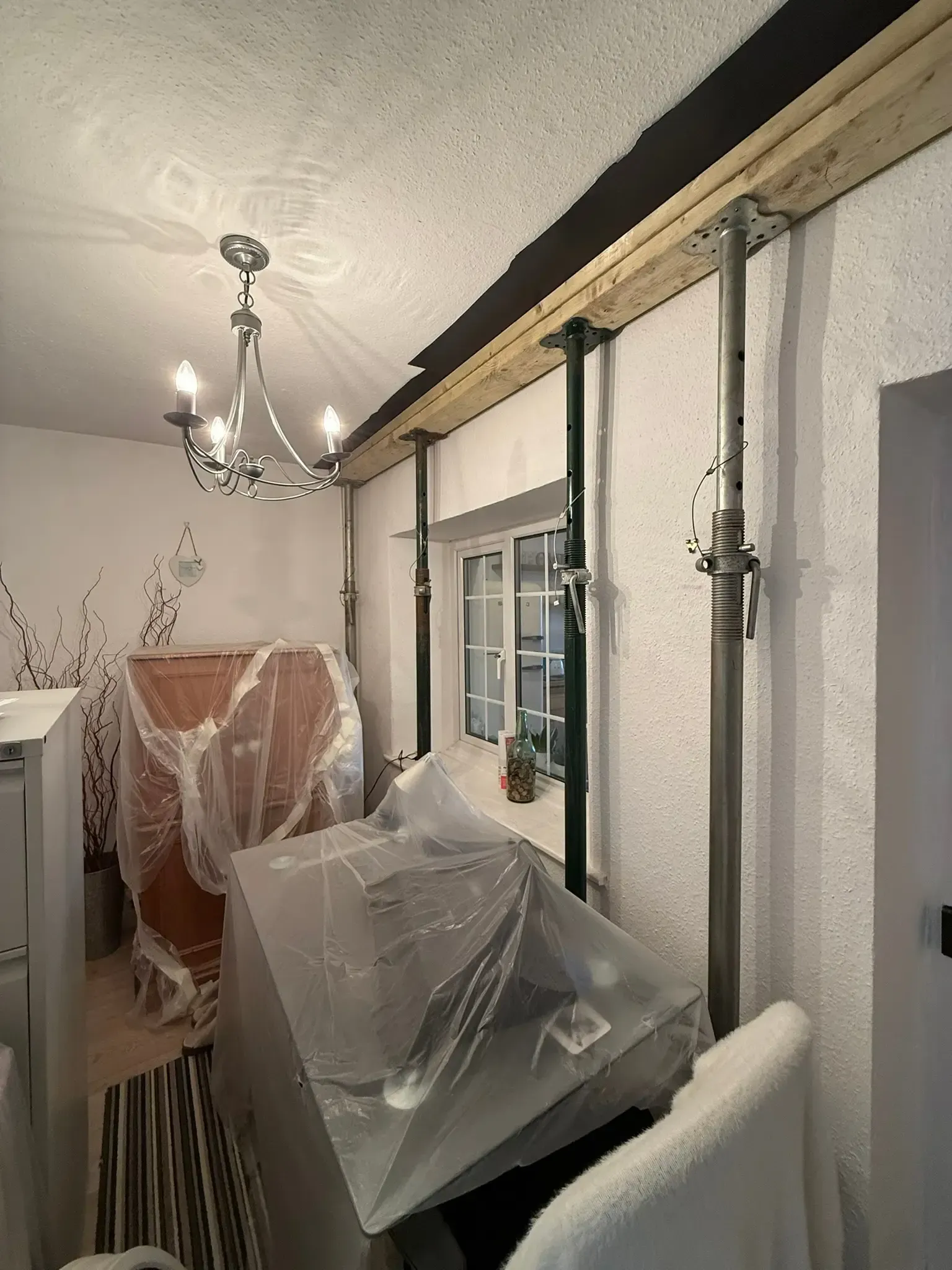 Cluttered dining room with furniture covered in plastic and exposed ceiling pipes along the wall