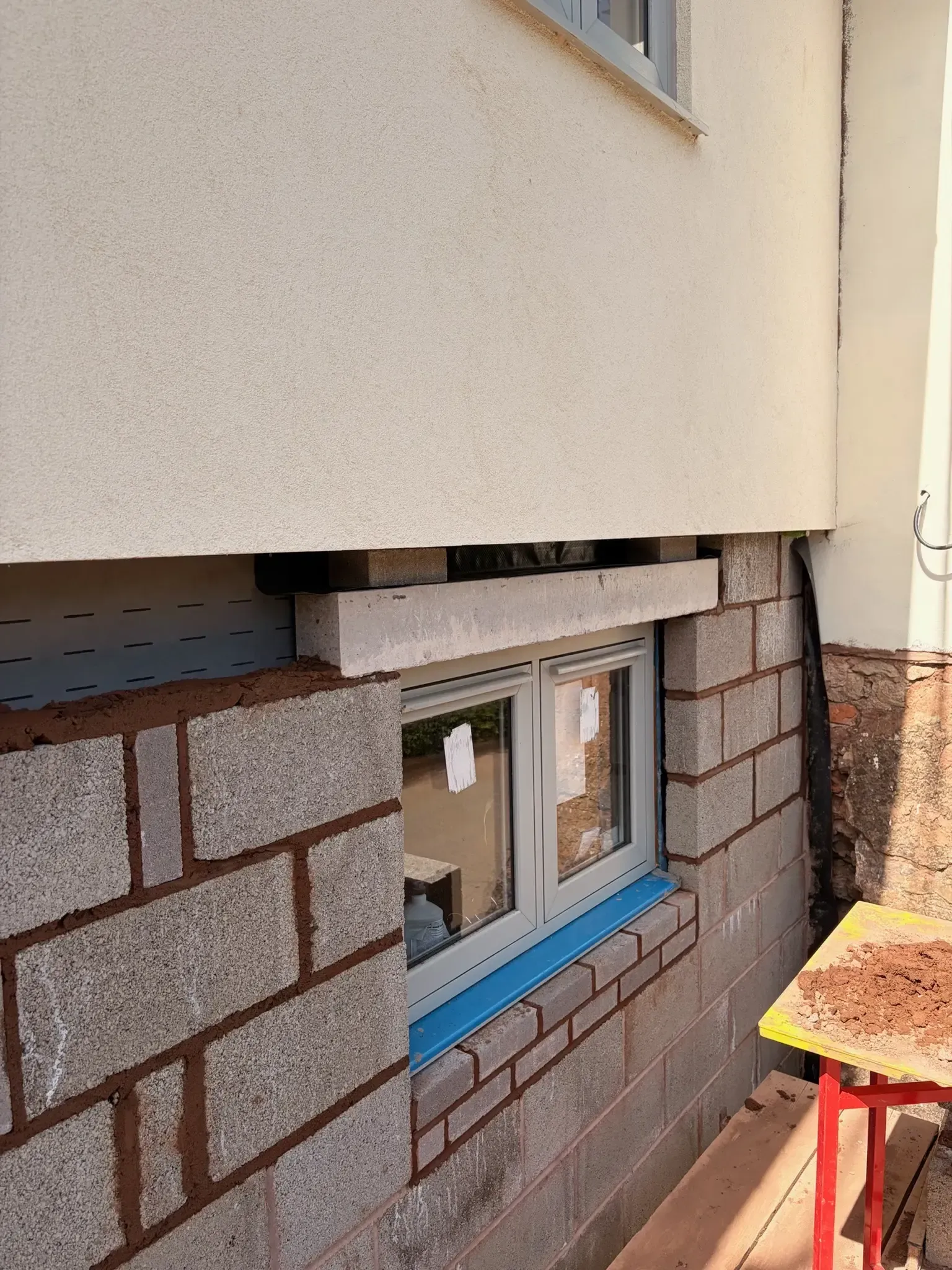 Partially finished exterior wall with exposed insulation, small window, and a red work table beside it