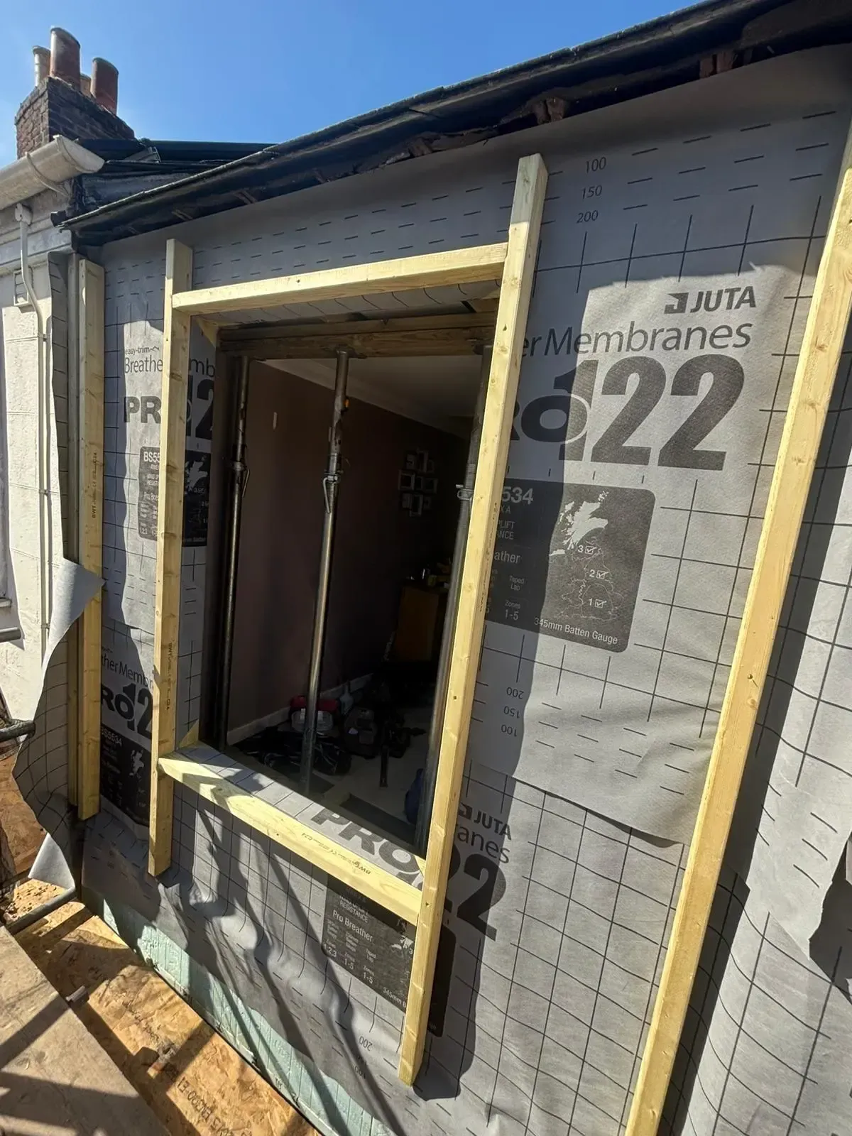Partially framed house window opening with house wrap, wood trim, and construction materials around it