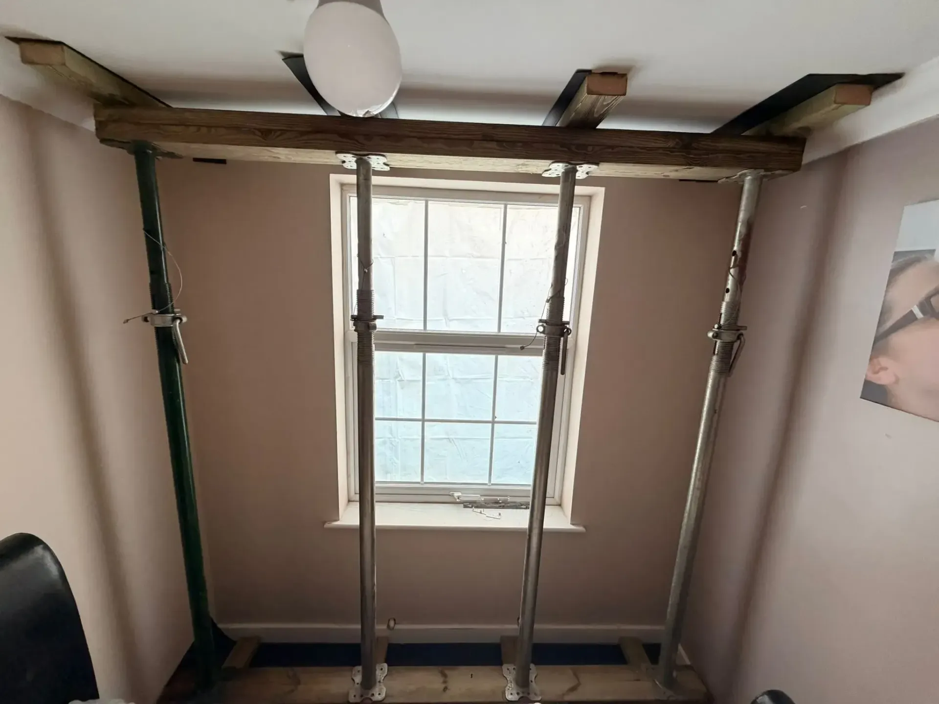 Room with a window and two wooden supports forming a temporary frame or scaffold inside.